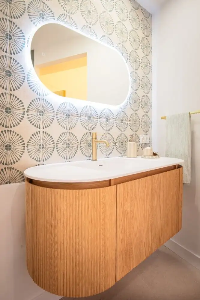 Contemporary bathroom with a wooden floating vanity, circular mirror with backlighting, and patterne.