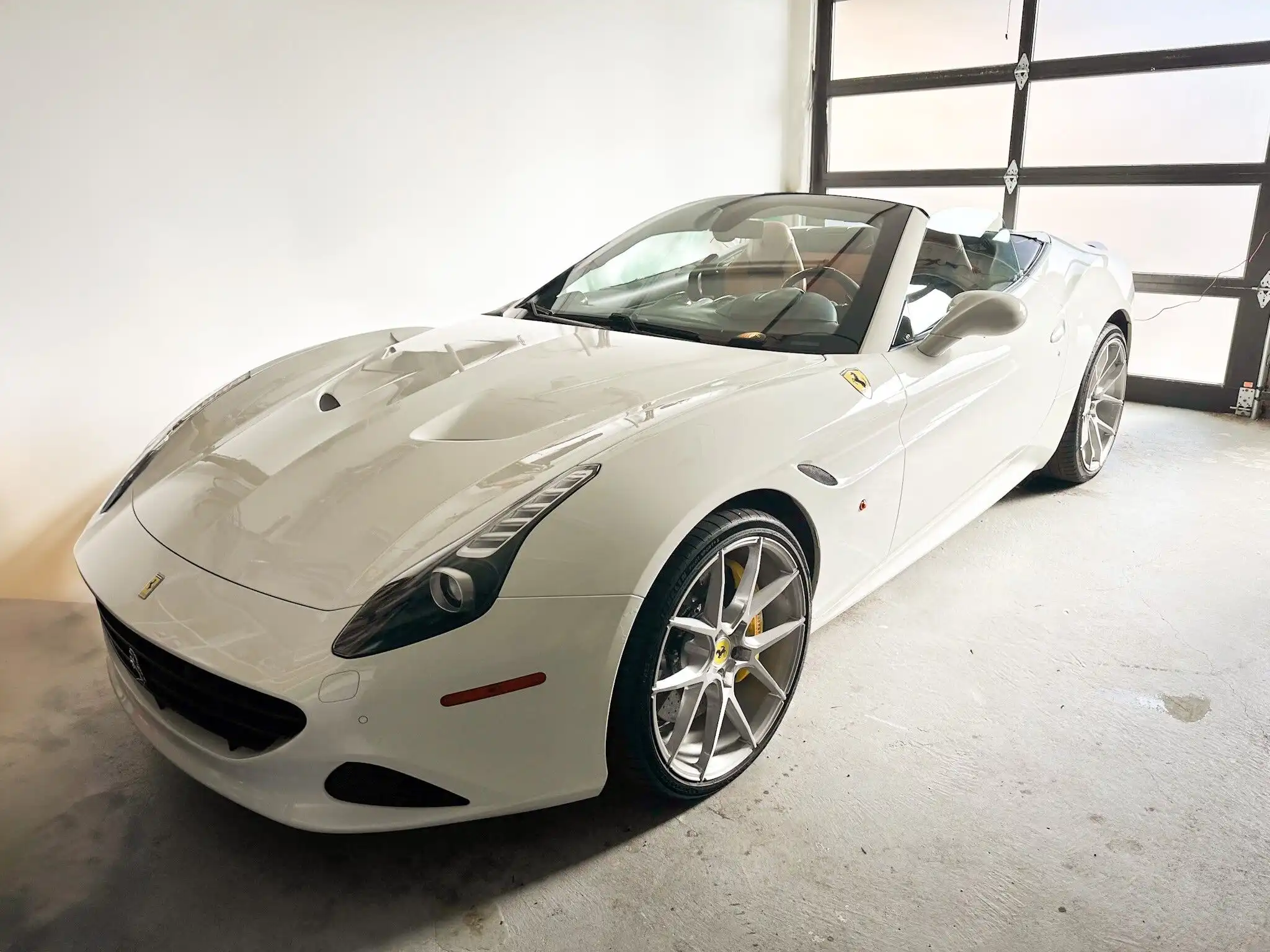 White luxury convertible sports car parked indoors with large garage door.