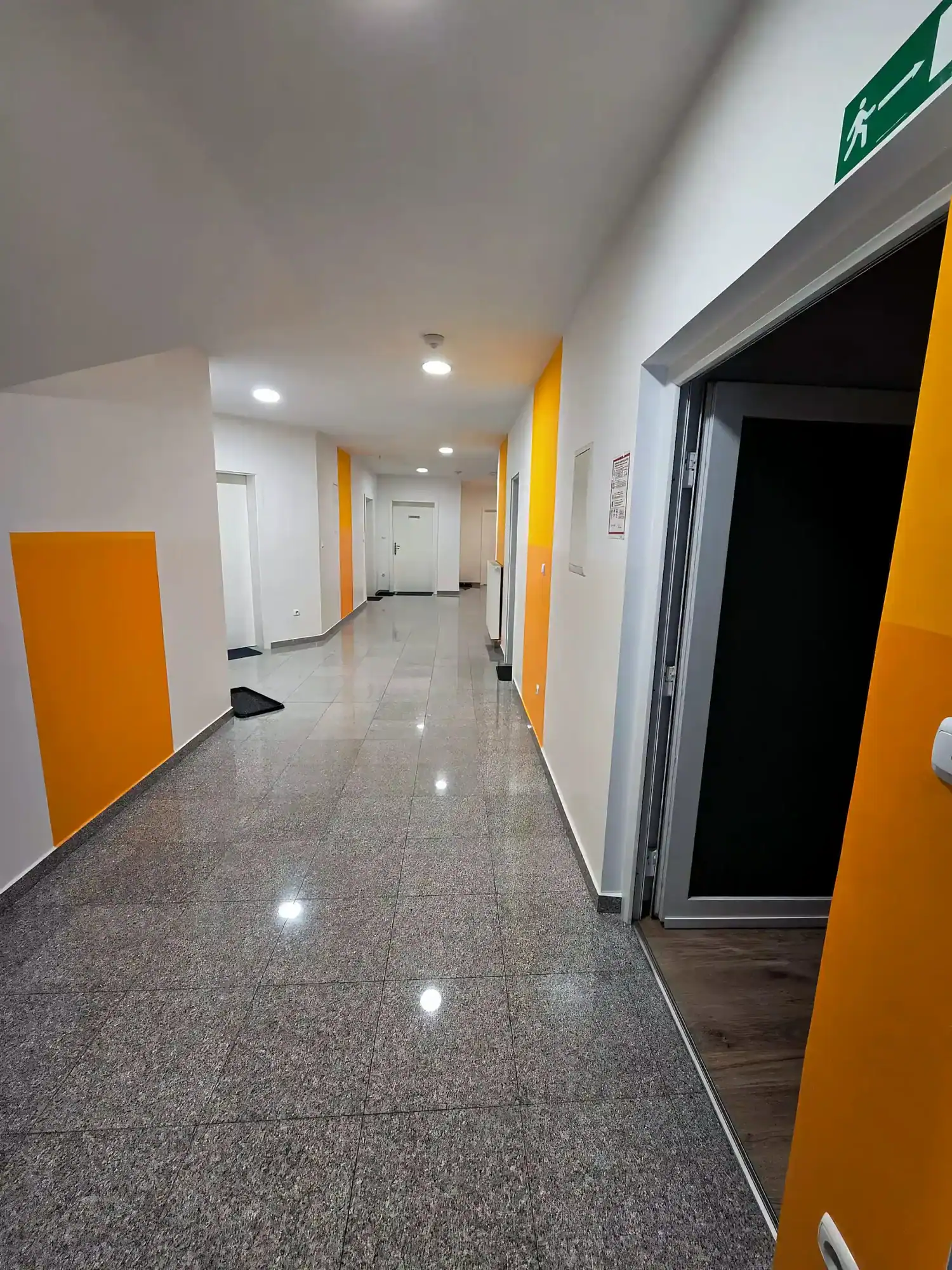 Bright commercial office hallway with yellow wall accents and elevator access.