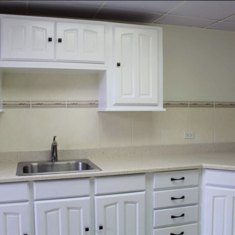 White kitchen cabinets with black handles and a stainless steel sink.