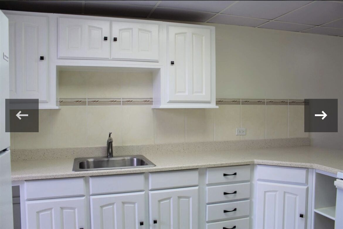 White kitchen cabinets with black handles and a stainless steel sink.