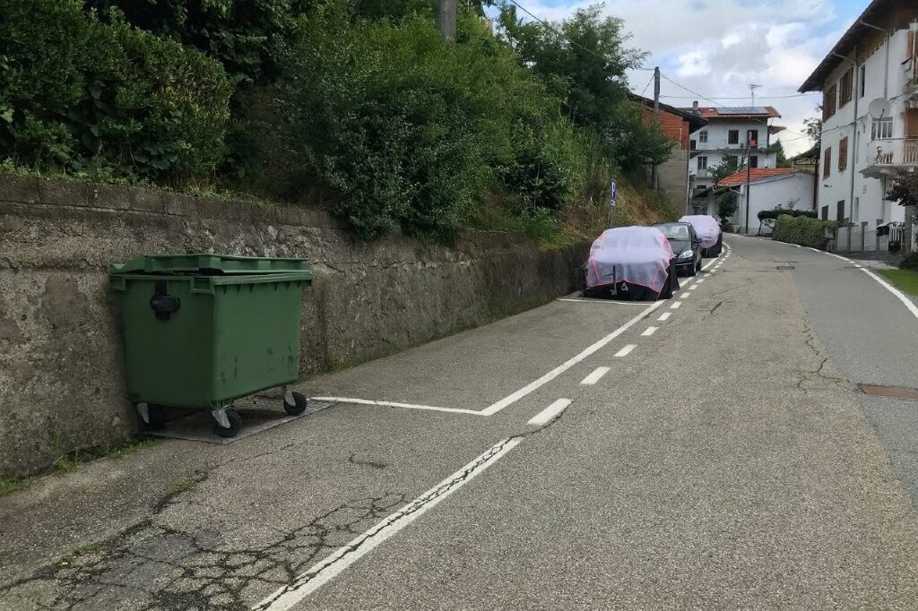 Charming Villa in Mezzana Mortigliengo Piedmont Parking area with cars and a green waste bin in a scenic Piedmont village setting.