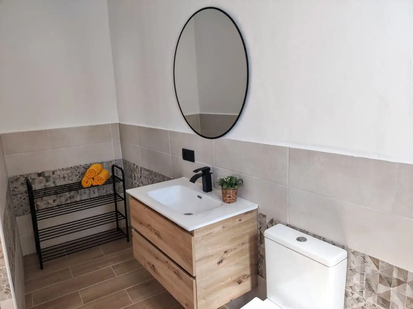 Modern bathroom featuring a wooden vanity, round mirror, and neutral tile decor.