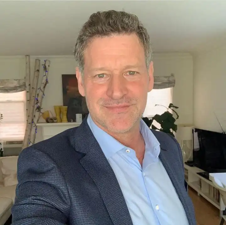 Portrait of a man in a blue suit and light blue shirt in a home setting.