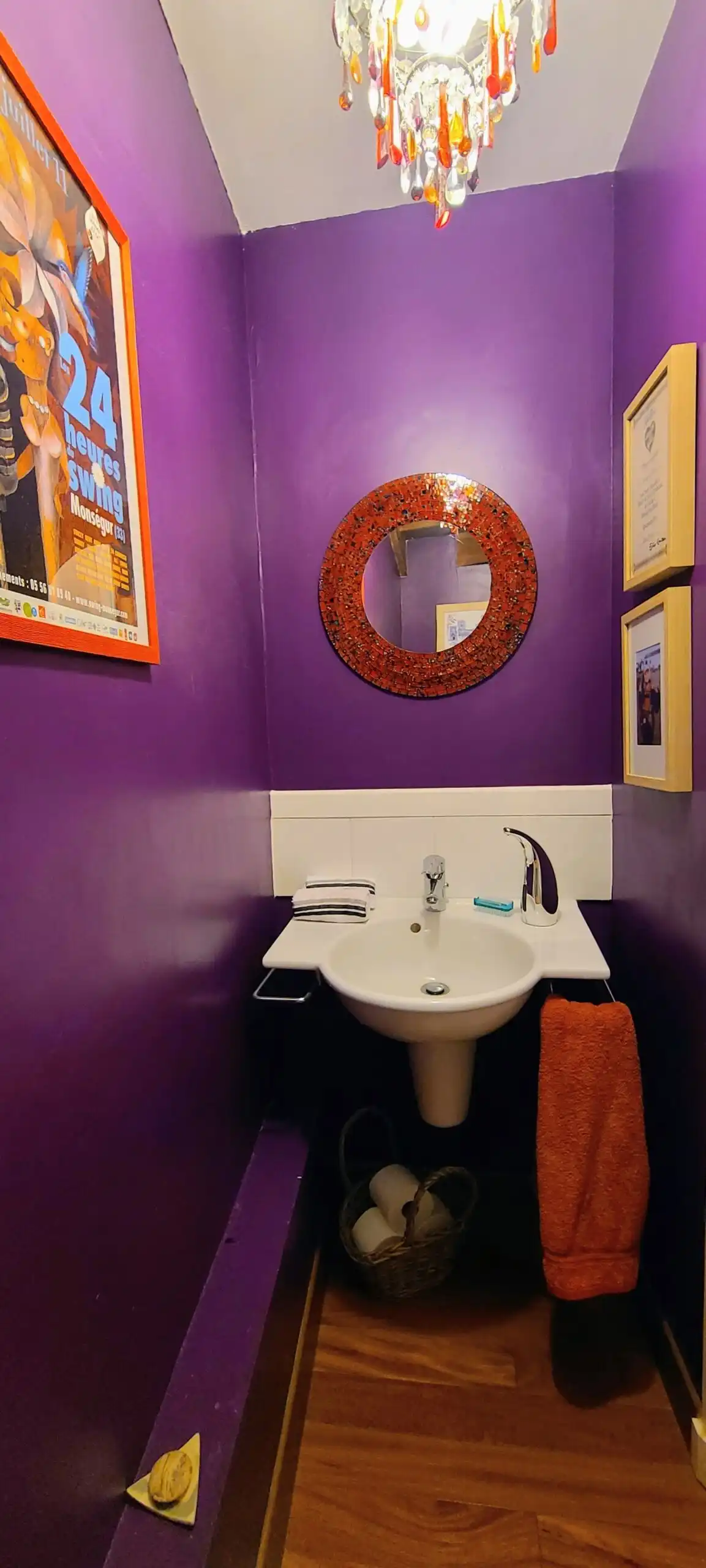 Bright purple bathroom featuring artwork, a mirror, and a small sink with towels and decor.