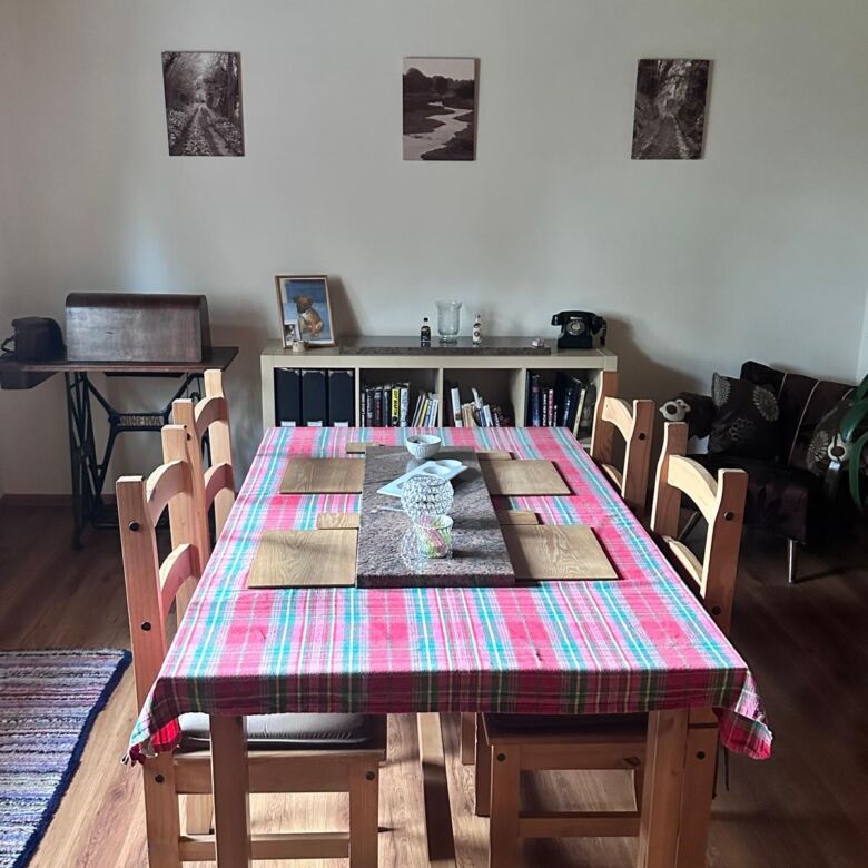 Spacious dining area featuring a wooden table with a colorful tablecloth, surrounded by matching cha.