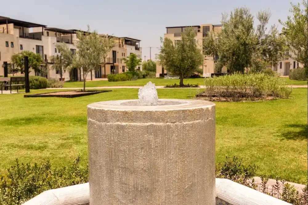 Beautiful outdoor space with a water fountain surrounded by trees and modern apartments.