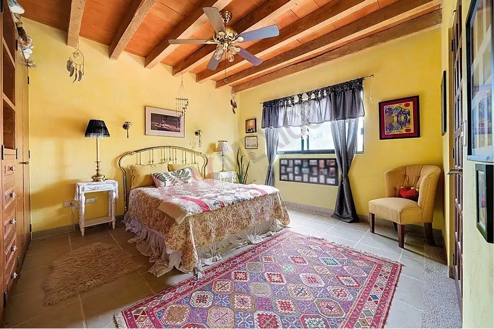 Style bedroom with vibrant yellow walls, wooden ceiling beams, and elegant furnishings in Rancho Los.