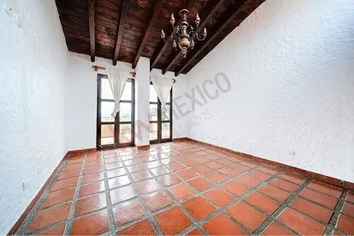 Interior view of a Spanish colonial estate featuring terracotta tile flooring and wooden ceiling bea.