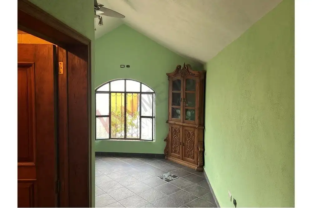 Interior view of a green room featuring a large window and antique wooden cabinet.