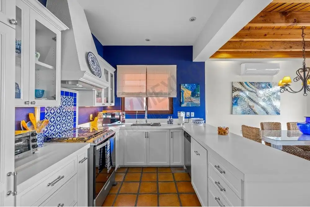 Level kitchen with white cabinetry and vibrant blue accent wall in Capilla de Piedra.