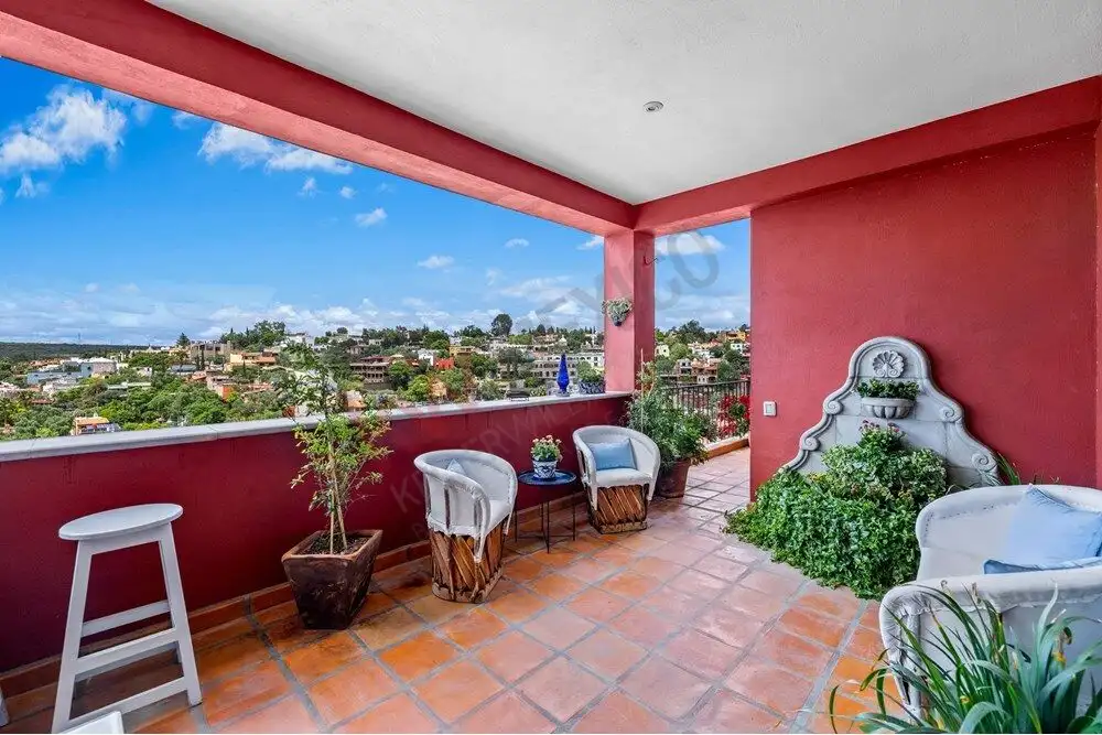 Balcony view of San Miguel de Allende with seating area and vibrant red walls.
