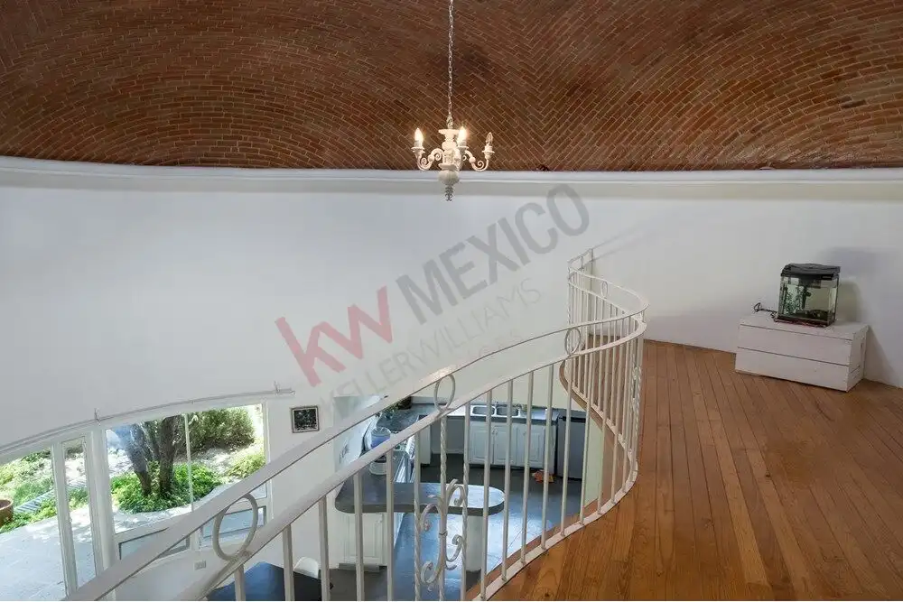 Modern staircase in a stylish home in San Miguel de Allende. Spacious interior with a curved staircase, high brick ceiling, and elegant chandelier.