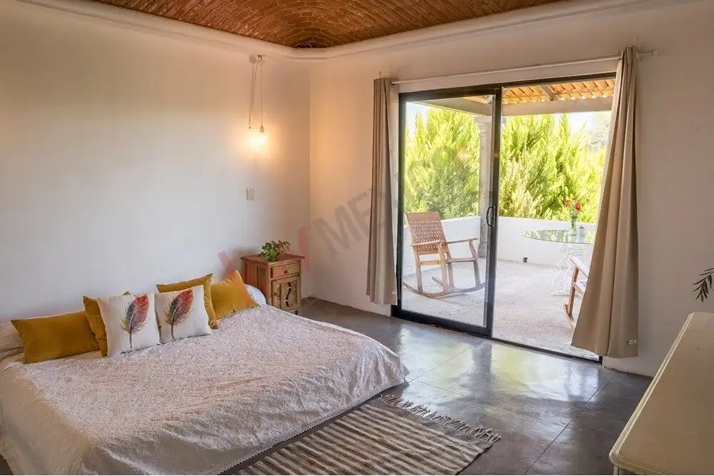 Modern bedroom with balcony view in Rancho Los Labradores, San Miguel de Allende. Spacious bedroom featuring a balcony with outdoor seating and lush greenery views.