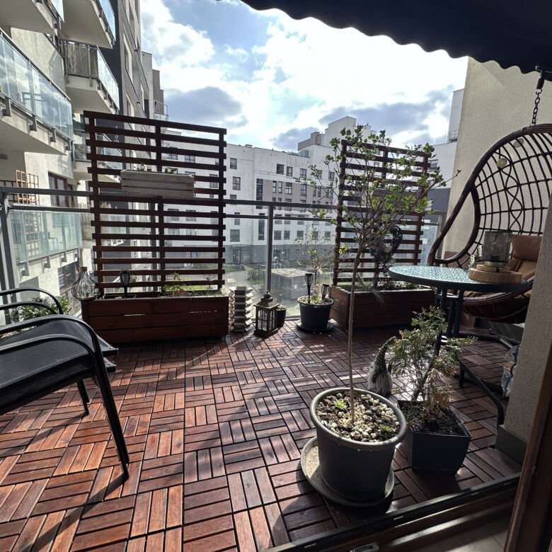 Balcony of a 2-bedroom apartment in Warsaw with plants, seating, and city views.