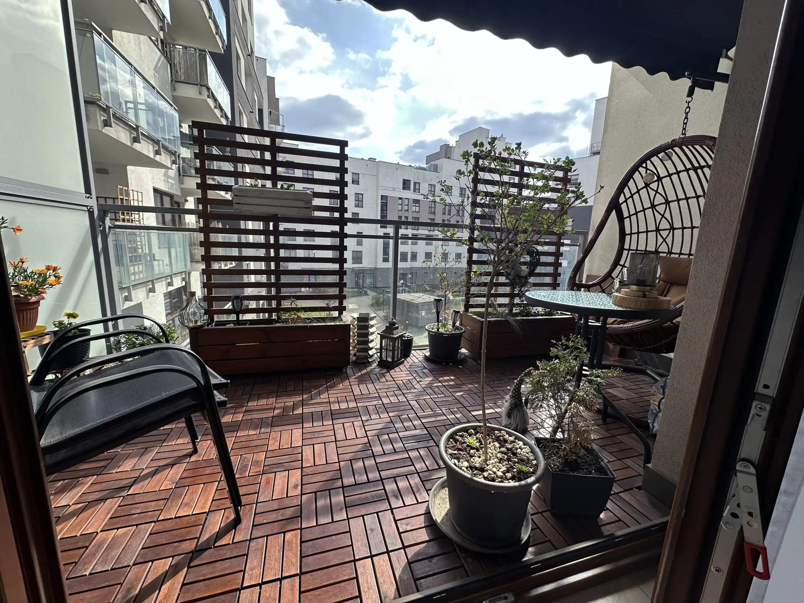 Balcony of a 2-bedroom apartment in Warsaw with plants, seating, and city views.