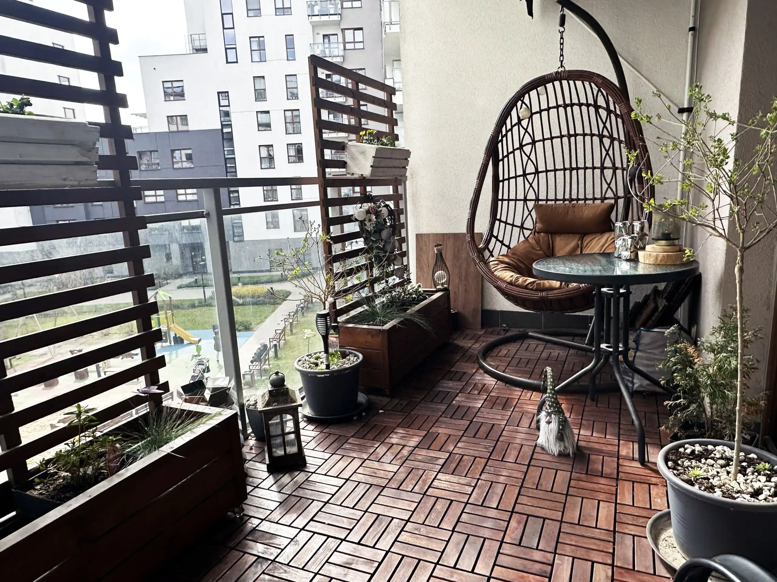 Modern Warsaw apartment balcony with cozy hanging chair and potted plants.