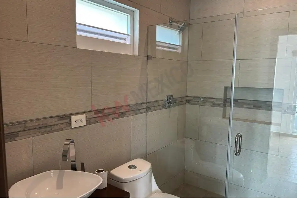 Modern bathroom with beige tiles and glass shower enclosure in a stylish home.