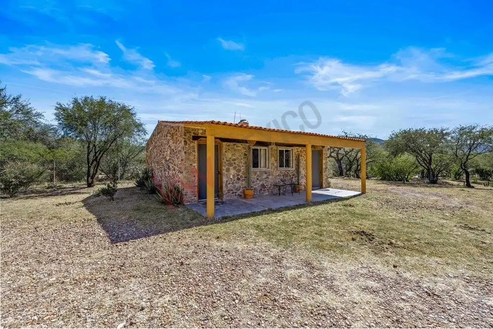 Rustic ranch house with stone walls and covered porch in rural setting.