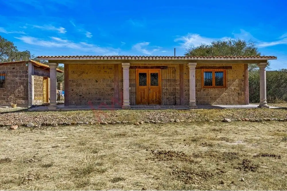 Ranch house with rustic stone walls, wooden doors, and a tiled roof in a rural setting.