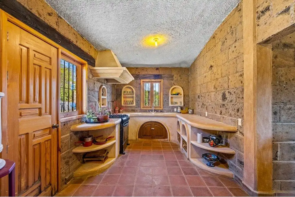 Rustic kitchen with stone walls, wooden cabinets, and natural light in a large country estate.