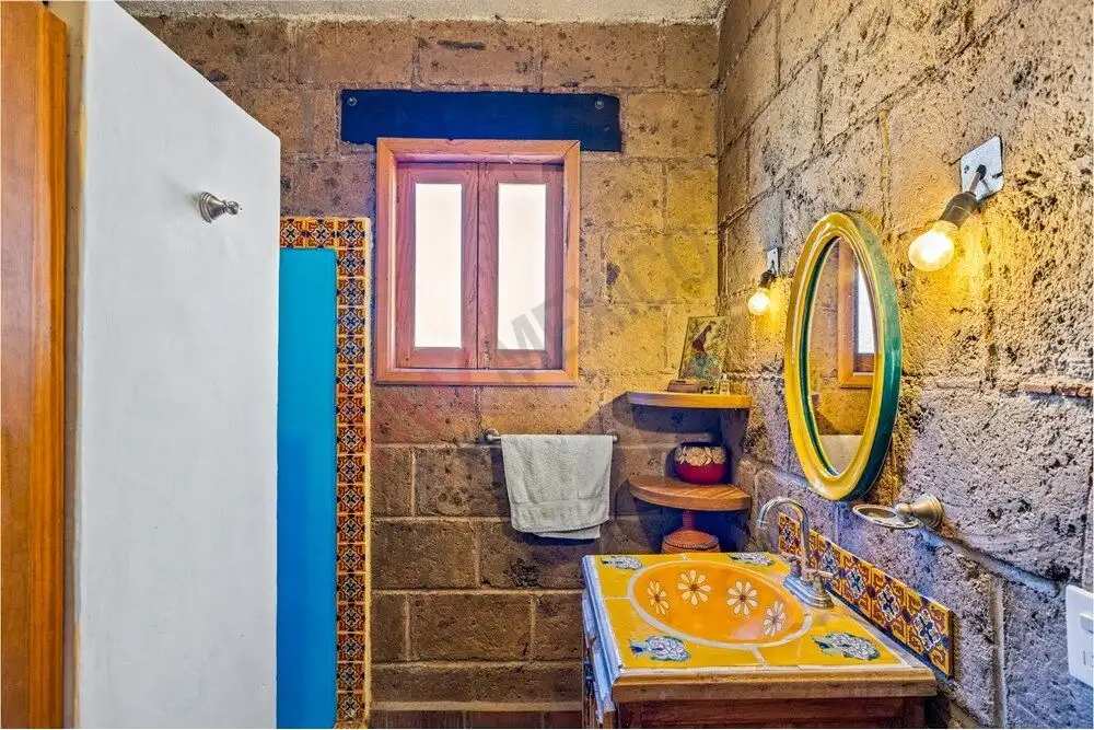 Bright rustic bathroom with stone walls, a small window, and vibrant yellow sink with decorative til.