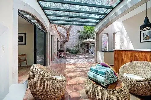 Outdoor patio with glass roof, wicker chairs, and lush garden view in Colonia Guadalupe.