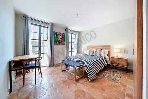 Cozy bedroom with large windows, wooden furniture, and terracotta tile flooring in San Miguel de All.