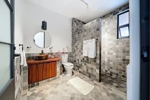 Bright bathroom featuring mosaic tiles, a wooden vanity, and a small window for natural light.