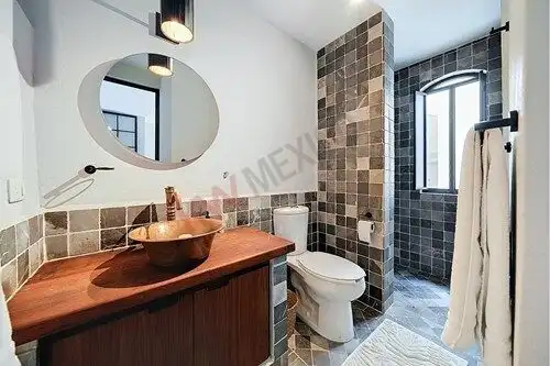 Modern bathroom with wooden vanity and tiled walls in a San Miguel de Allende home.