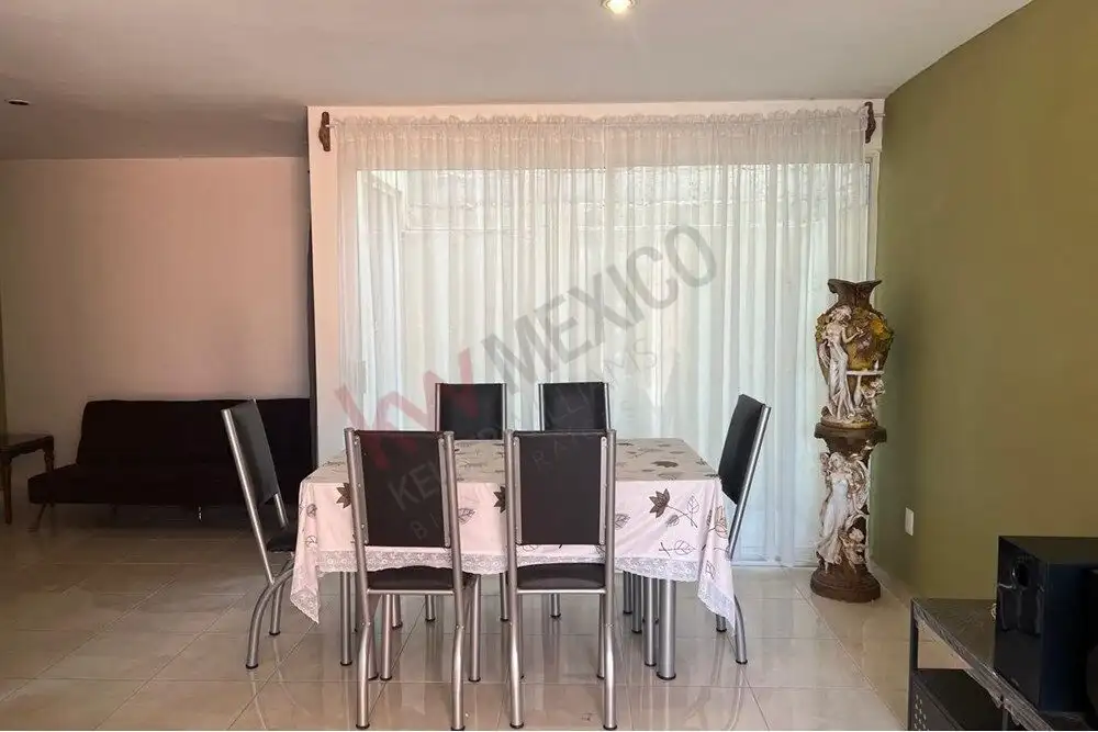 Modern dining room with large window and elegant decor in Guadalupe Mexiquito. Spacious dining area with six chairs, a floral tablecloth, and decorative vase.