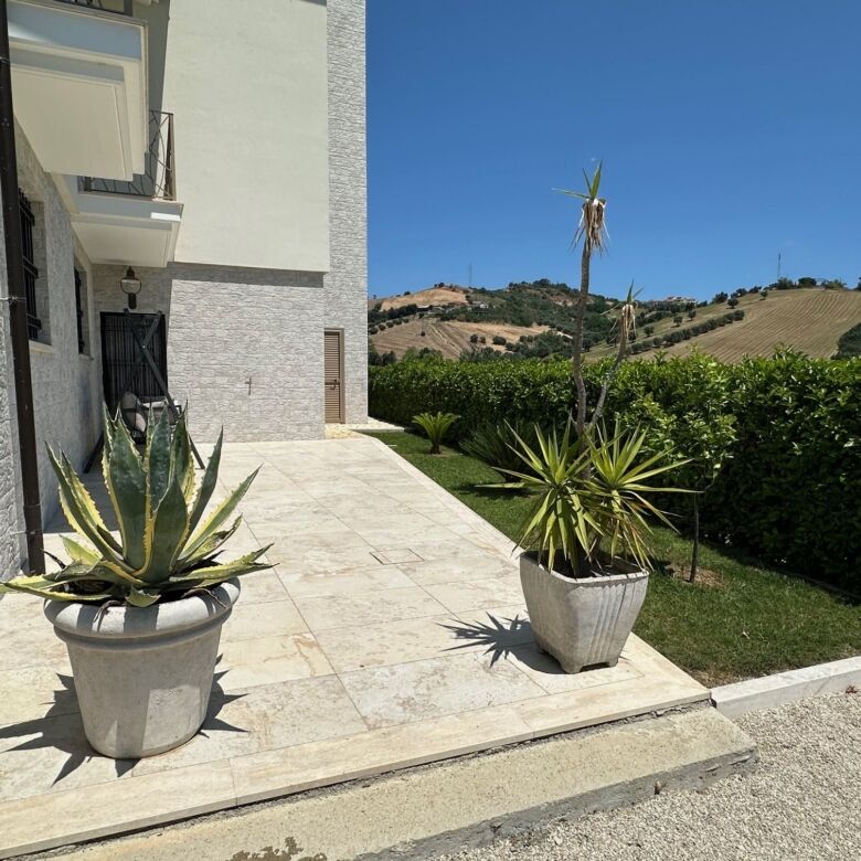 Elegant villa entrance with potted plants and scenic countryside view.