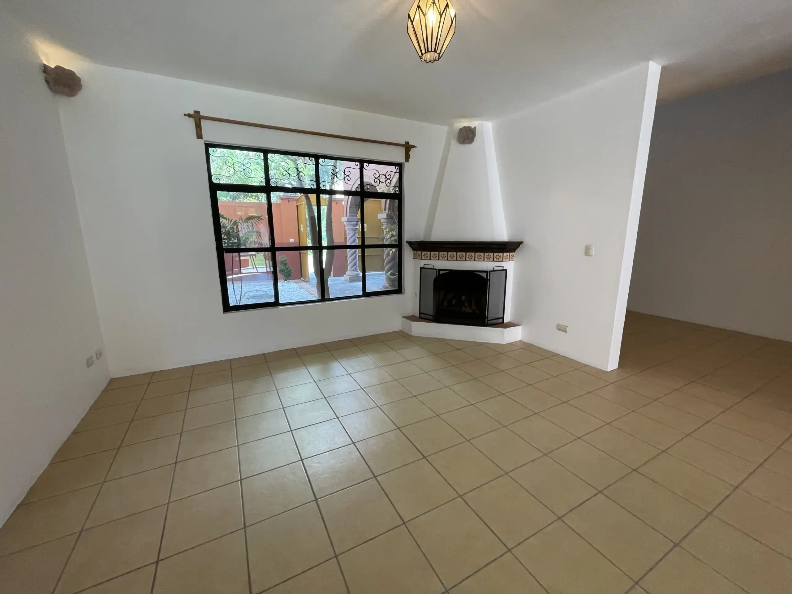 Spacious living area featuring a fireplace, tiled flooring, and a large window with garden views.