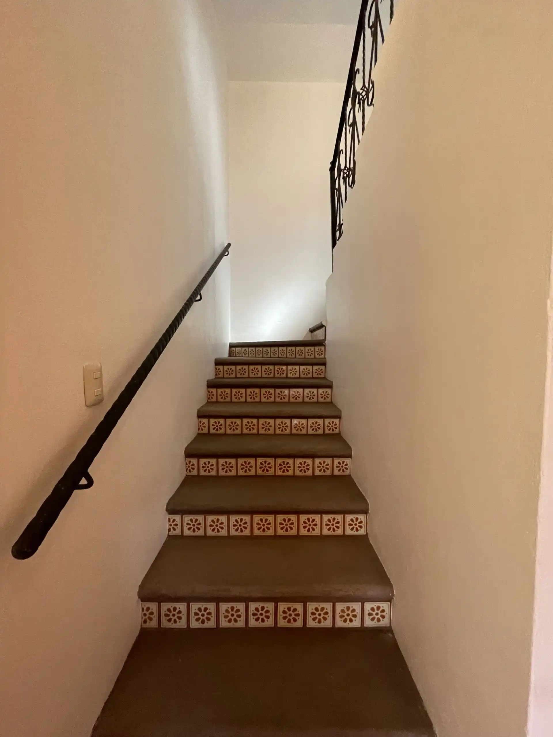Indoor staircase featuring patterned tile risers and a black handrail, leading to the upper floor of.