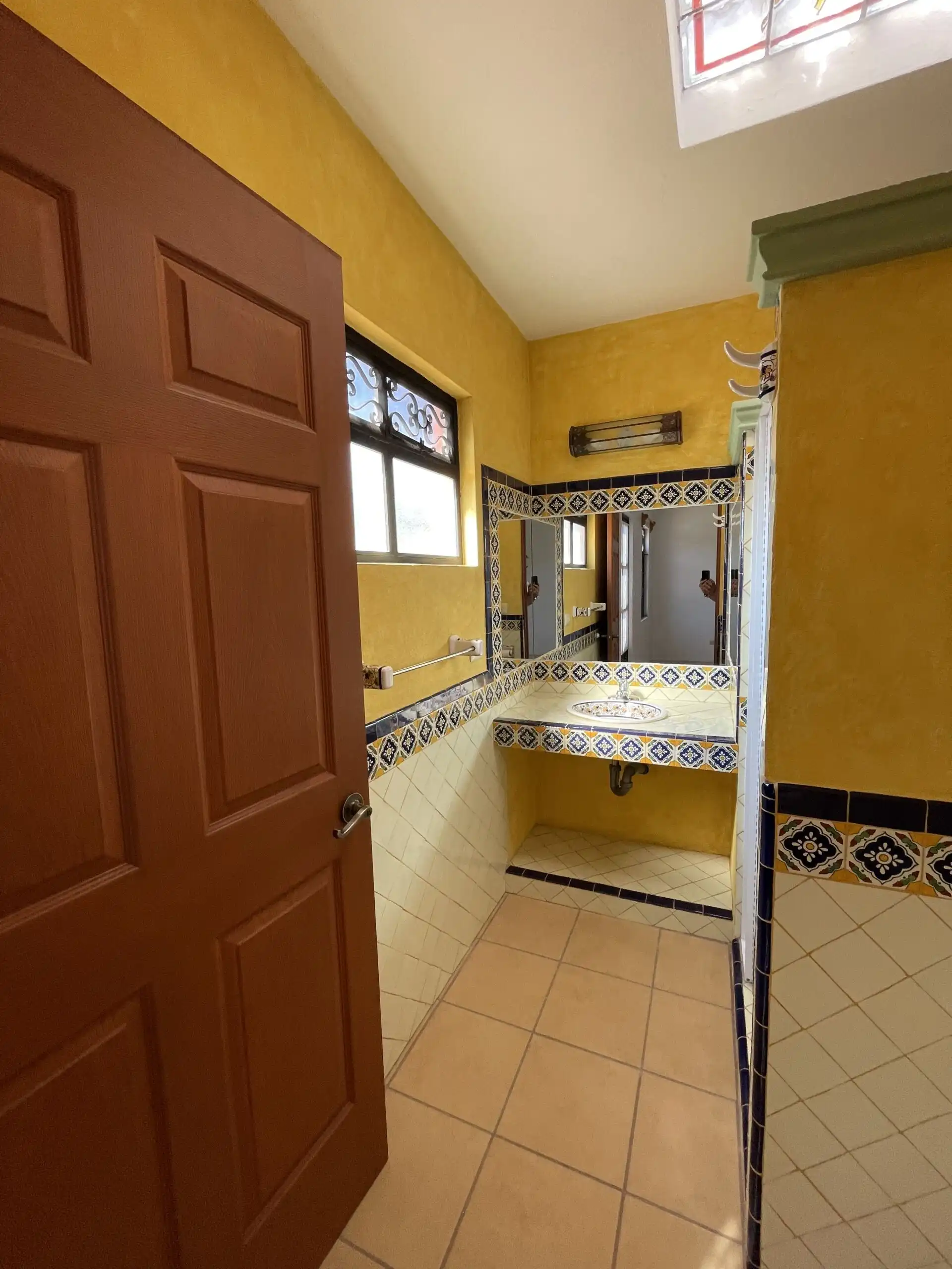 Bright bathroom featuring vibrant yellow walls, decorative tile accents, and a window providing natu.