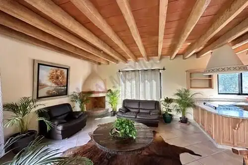 Spacious living area featuring wooden beam ceiling, cozy fireplace, and lush indoor plants in Rancho.