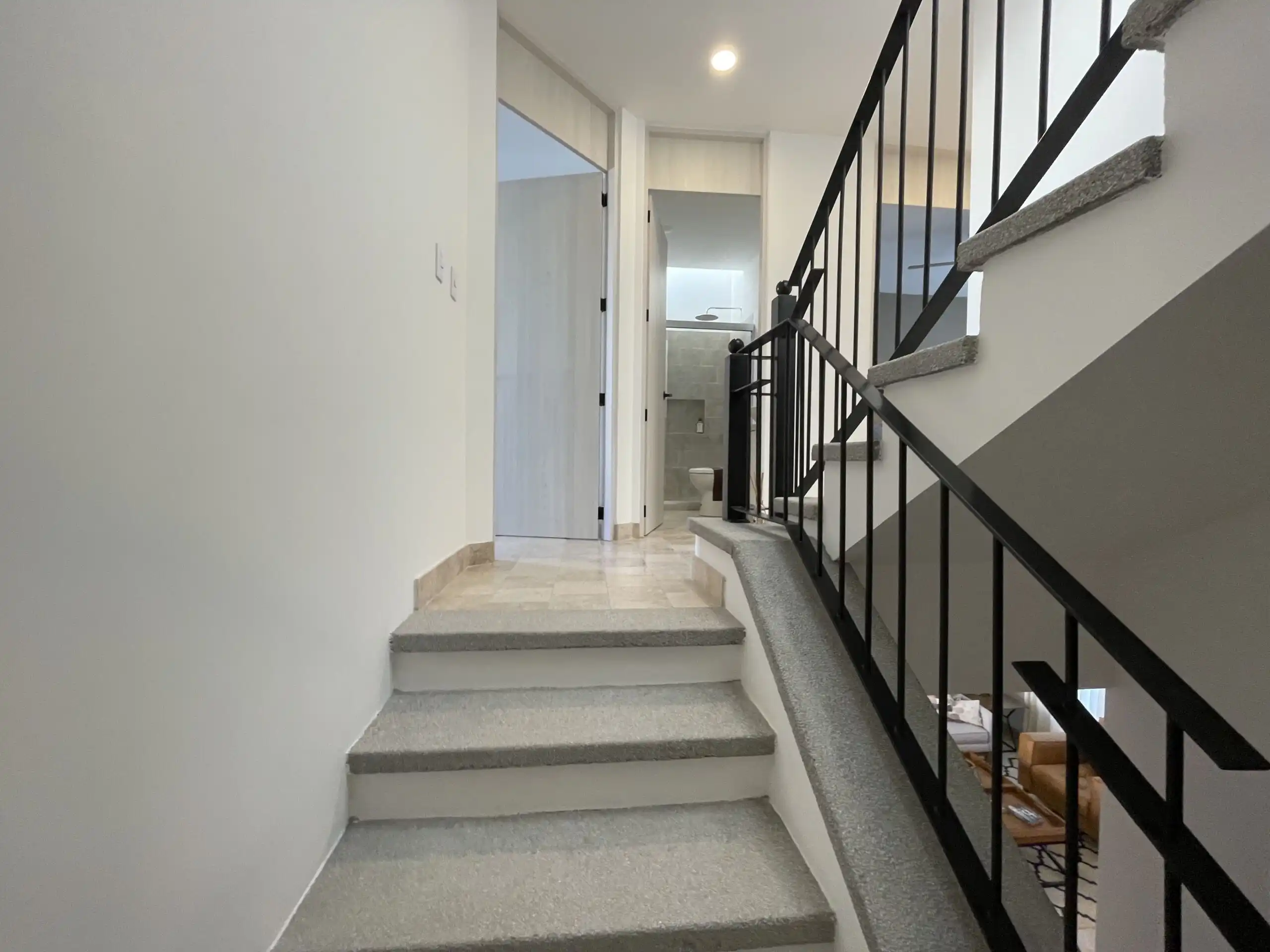 Interior view of a modern home featuring a staircase, clean white walls, and a hallway leading to ot.