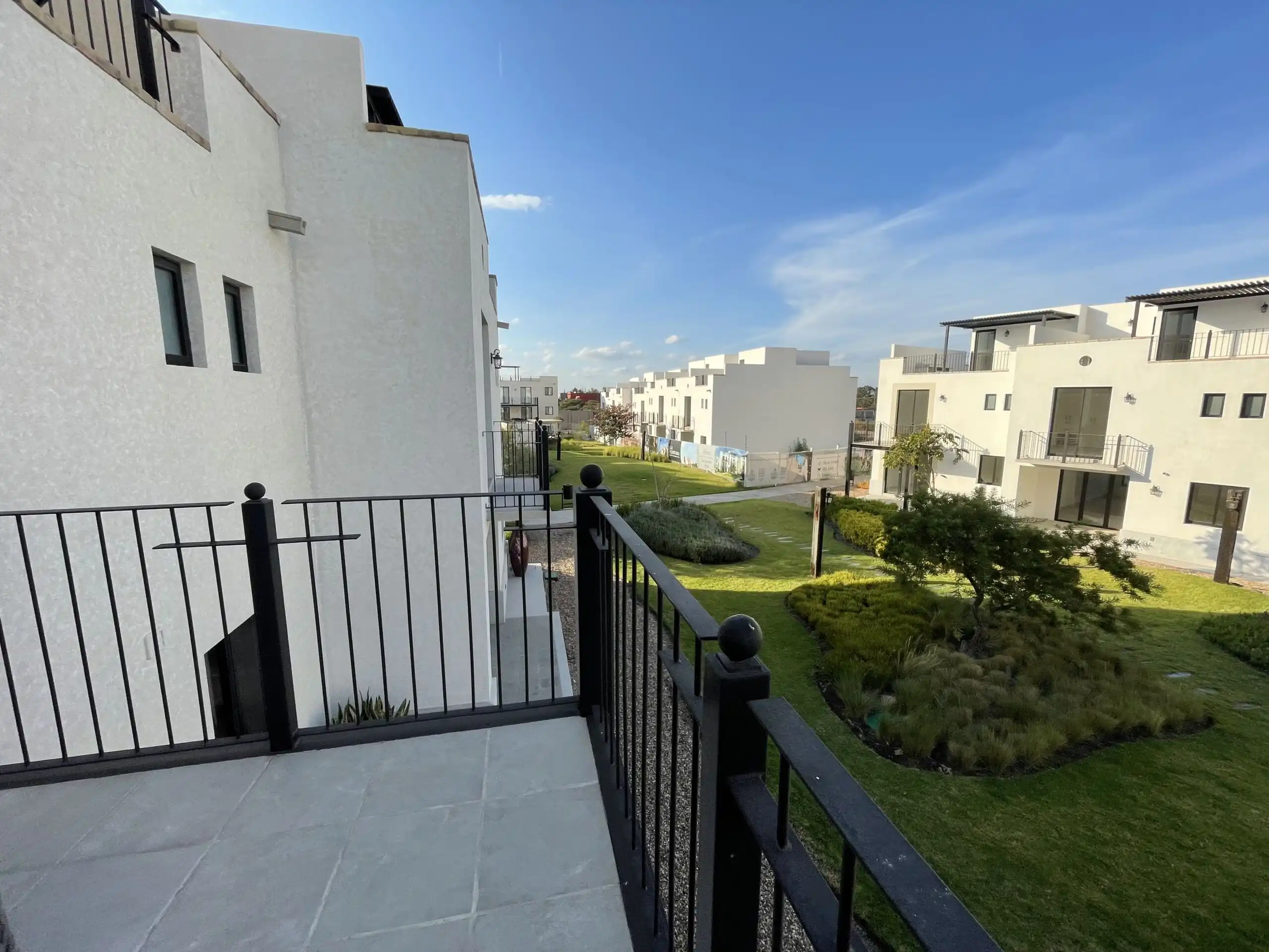 View of a modern residential building with a balcony overlooking a landscaped garden under a clear b.