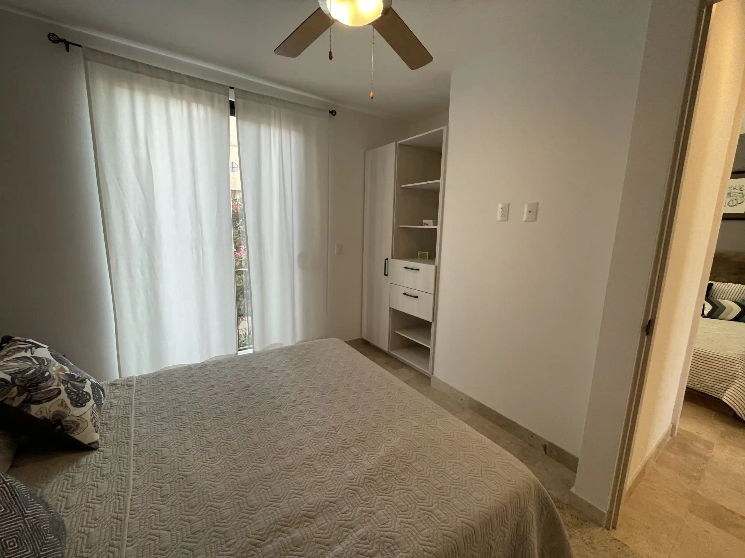 Bright bedroom featuring large windows with sheer curtains and a cozy bed with patterned pillows.