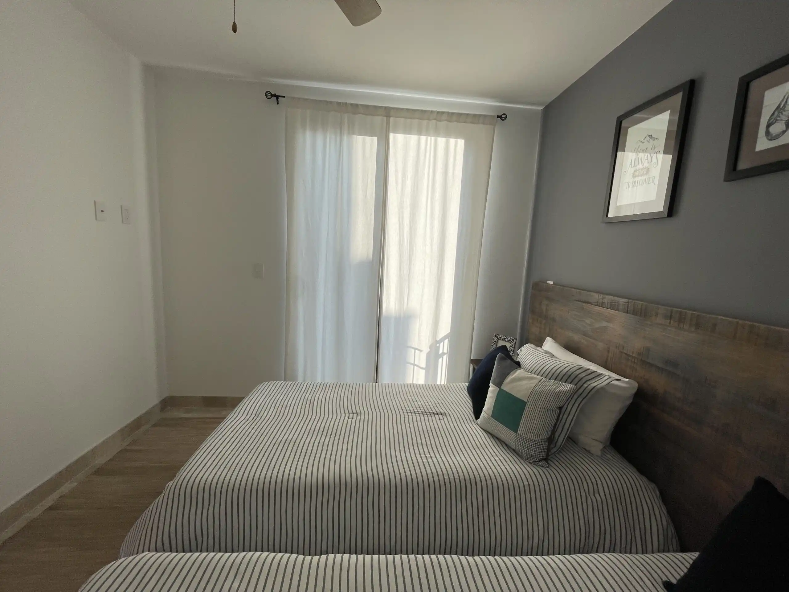 Beautiful bedroom featuring large windows with sheer curtains, a comfortable bed with decorative pil.