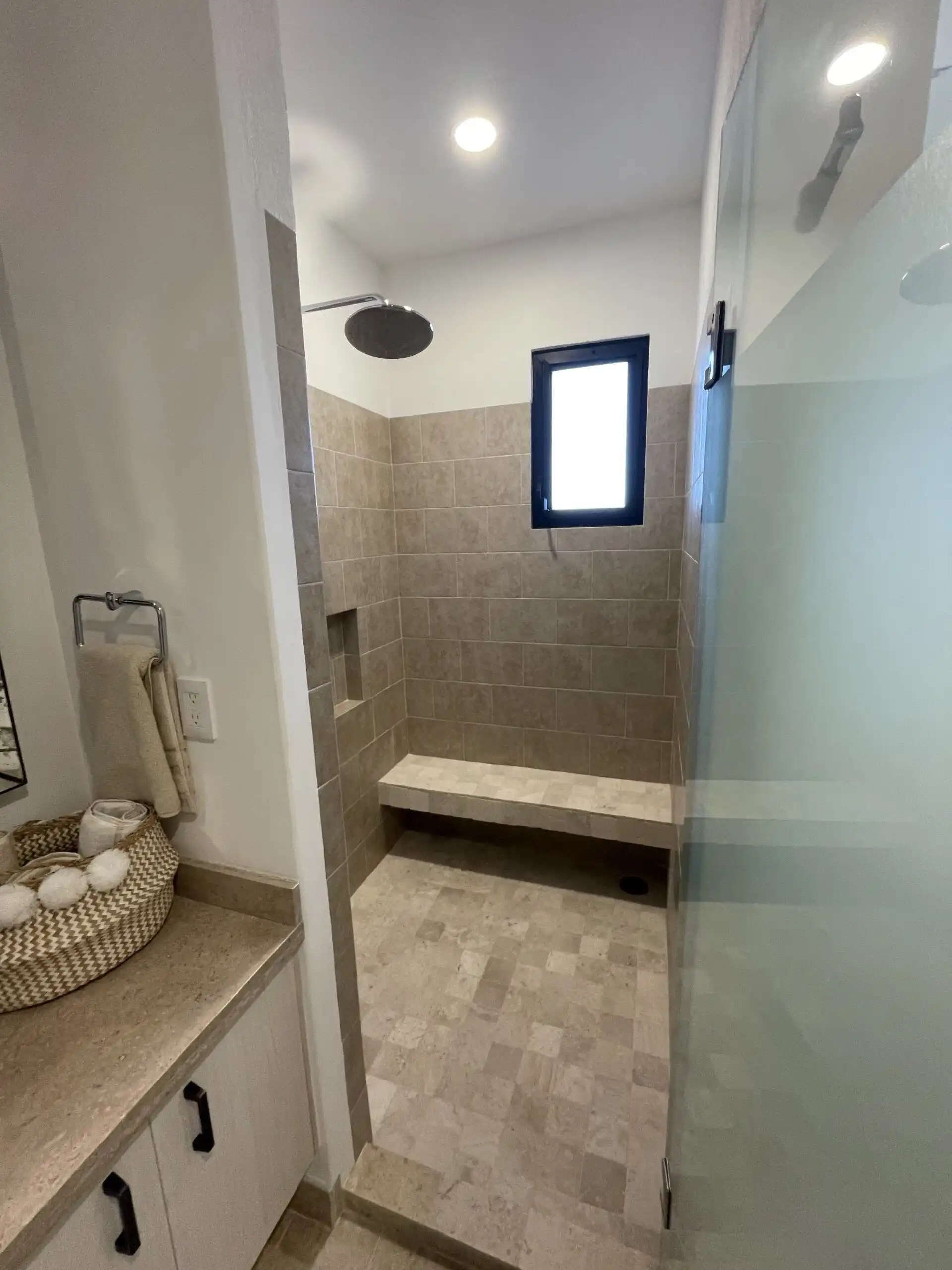 in shower with beige tiles and a built-in bench in a luxury home. Luxury home walk-in shower with beige tiles and a small window.