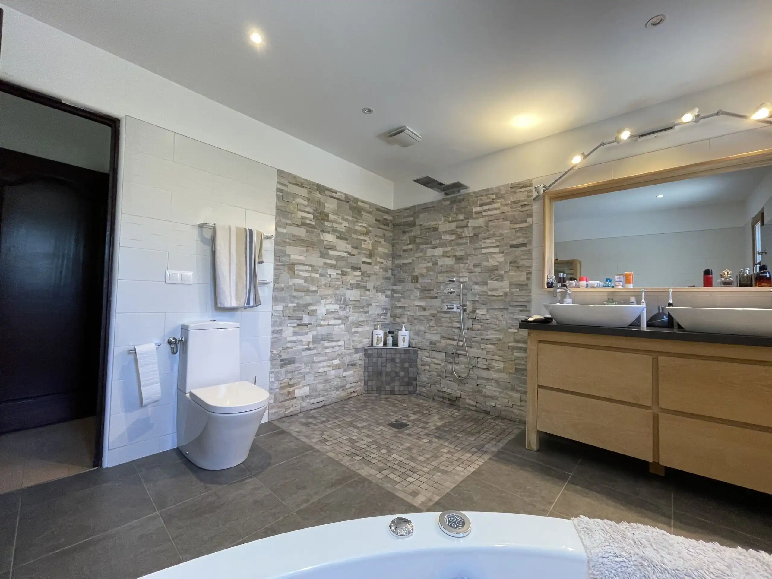 Spacious bathroom with modern fixtures, stone wall accents, and a large mirror in a luxurious Biot v.