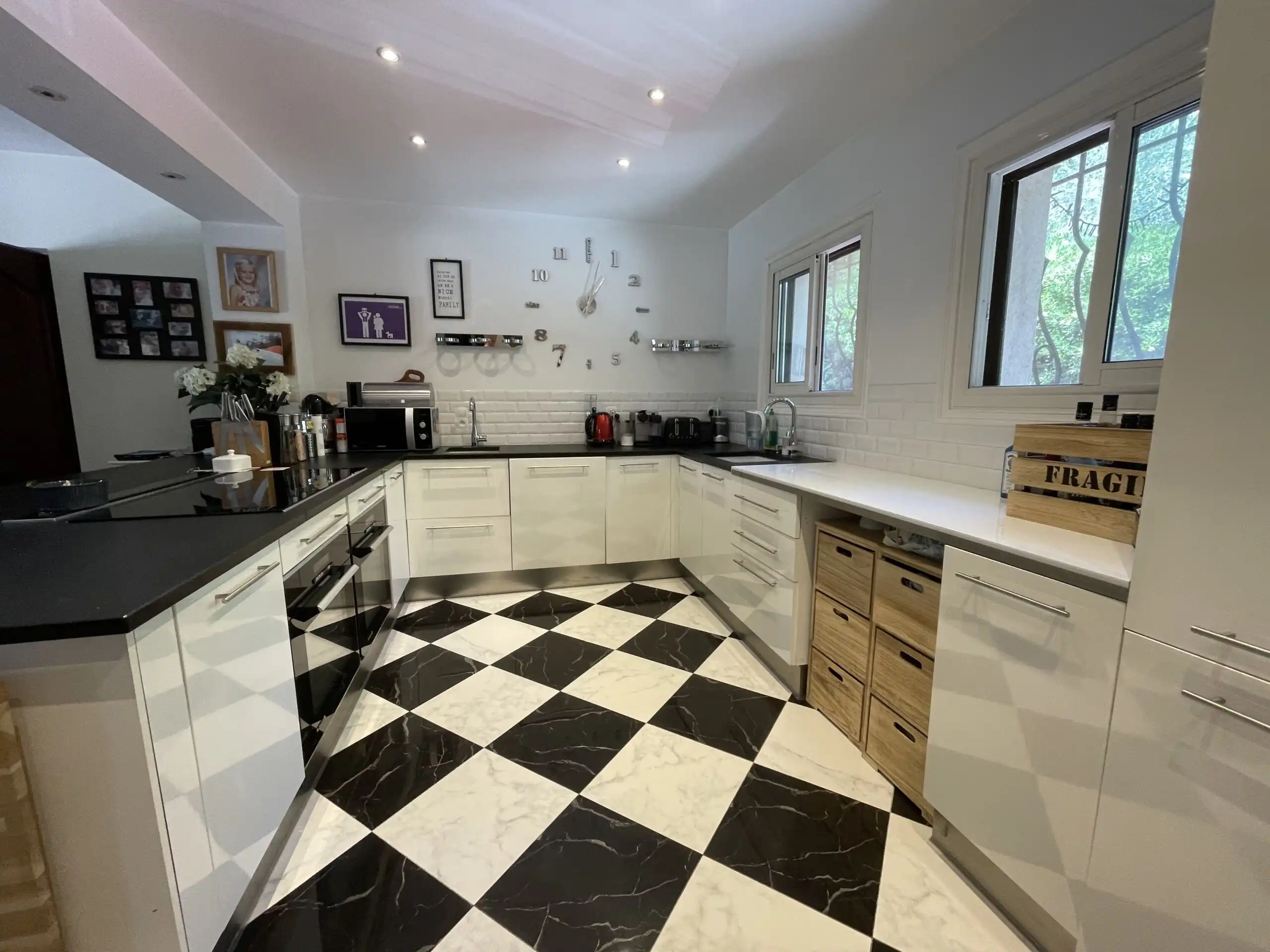 Spacious kitchen with white cabinets, black countertops, and large windows overlooking greenery.