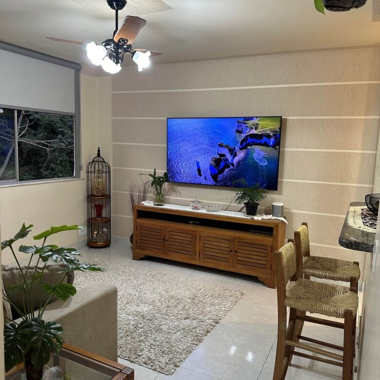 Bright living room with a wall-mounted TV, wooden furniture, and large window for natural light.