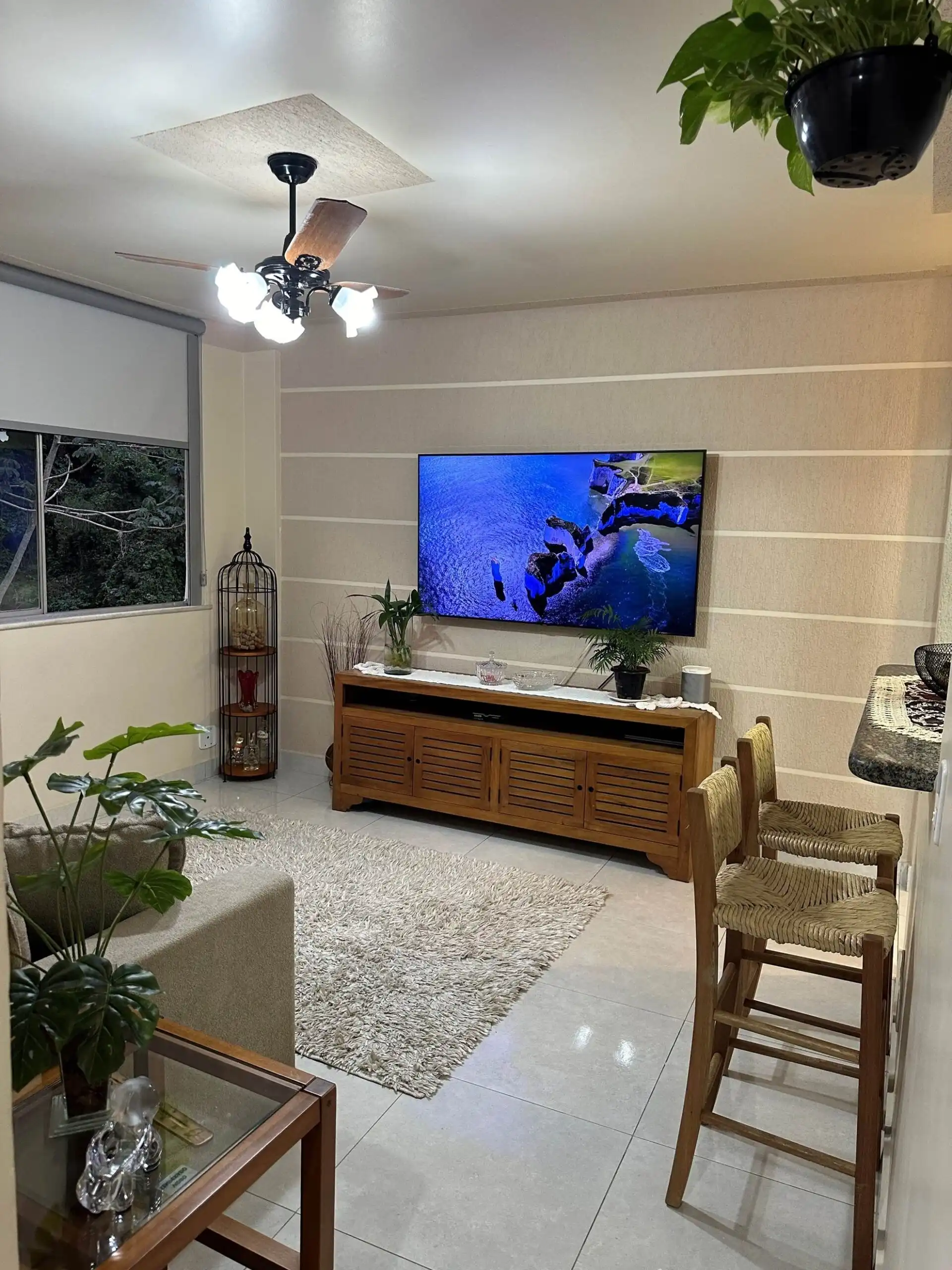 Modern living room with TV and natural light Bright living room with a wall-mounted TV, wooden furniture, and large window for natural light.