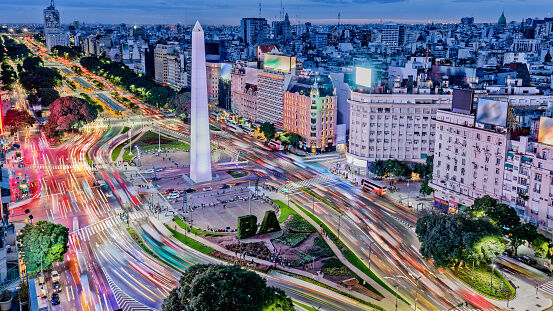 Brightly lit Buenos Aires city center with traffic and tall skyscrapers at night.
