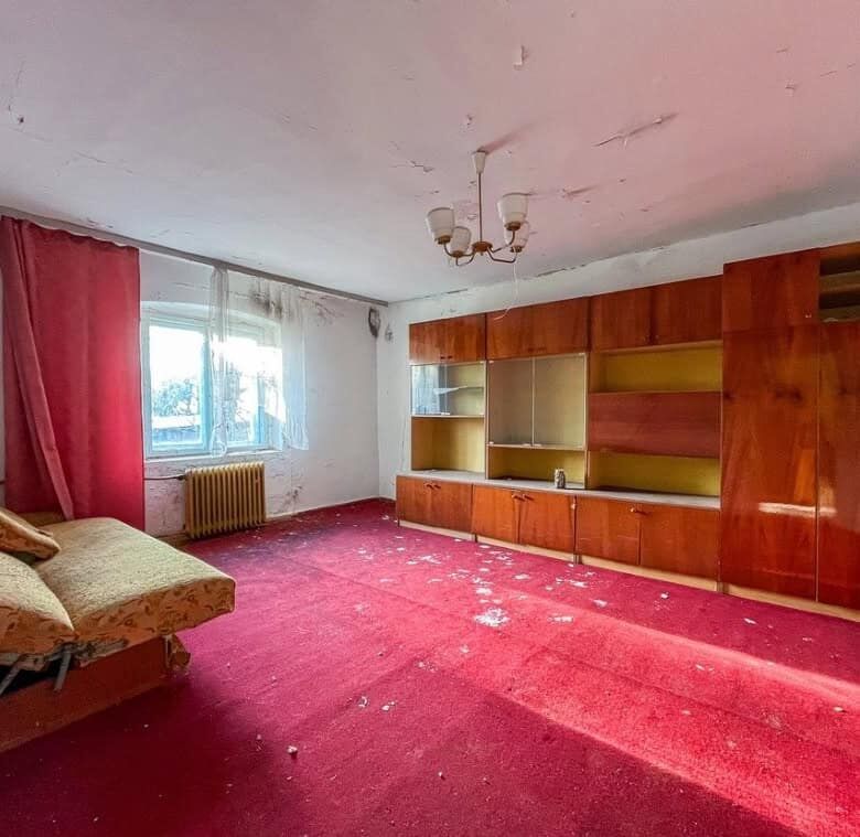 Interior of a large living room with red carpet, wooden shelving, and a window with curtains in Lubi.