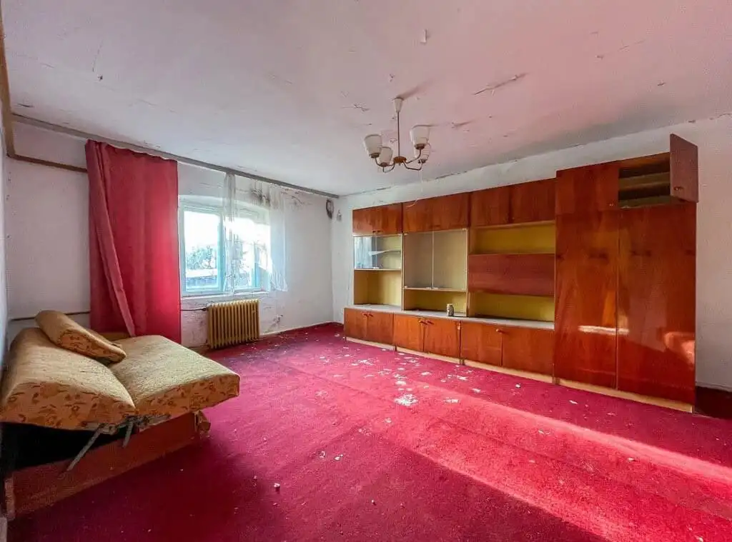 Interior of a large living room with red carpet, wooden shelving, and a window with curtains in Lubi.