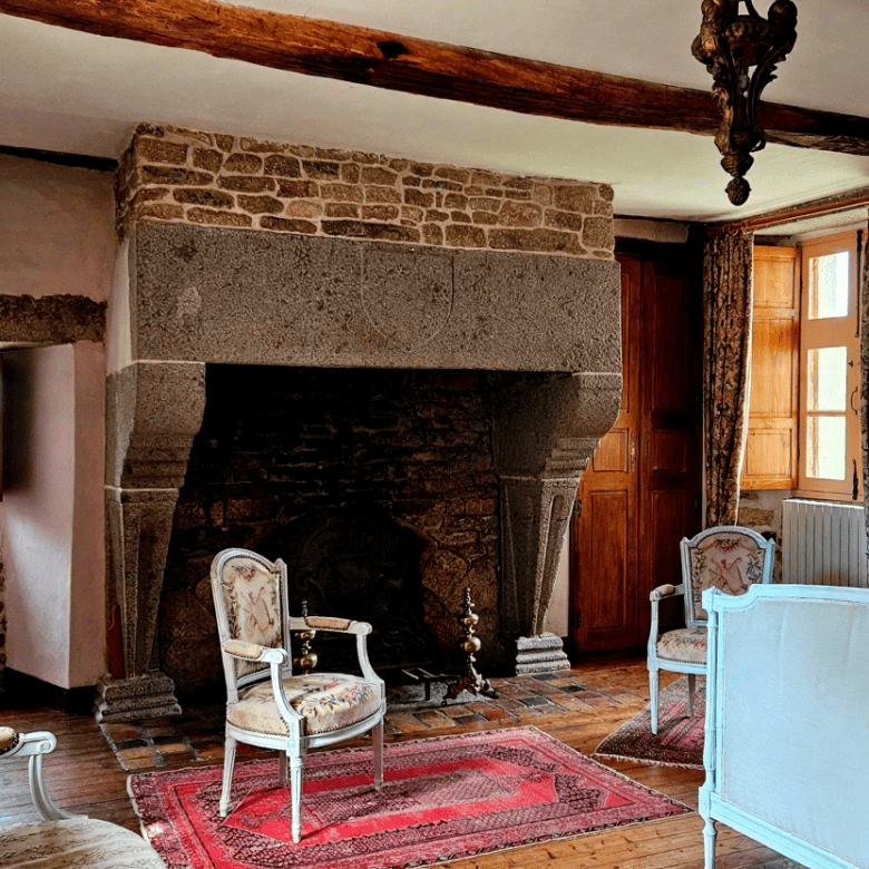 Charming interior of Le Manoir de Dougeru with rustic stone fireplace and vintage furniture.