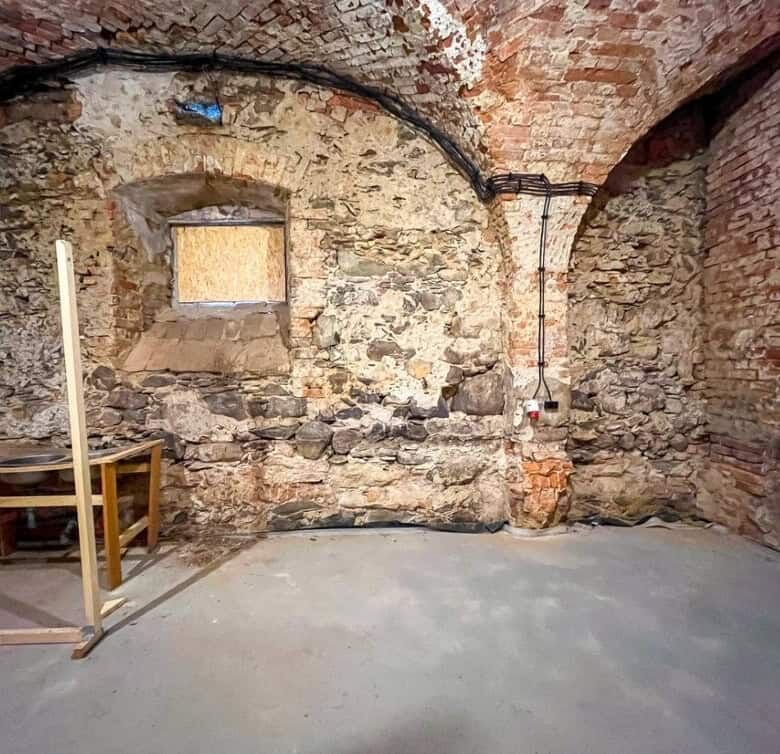 Ancient stone cellar with brick arches, small window, and unfinished floor.